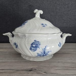 Può includere: Zuppiera in porcellana bianca con coperchio, ornata da motivi floreali blu. La zuppiera presenta una maniglia decorativa sul coperchio e manici laterali. Il design include un motivo a reticolo e una base a piede, adatta per servire zuppe o stufati.