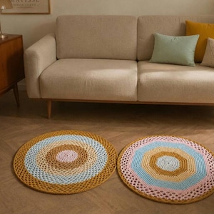 Puede incluir: Dos alfombras circulares de ganchillo con patrones concéntricos en tonos amarillo mostaza, azul claro y rosa suave. La alfombra de la izquierda tiene un centro sólido, mientras que la de la derecha muestra un diseño geométrico octogonal con borde calado.