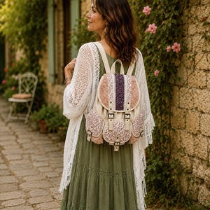 May include: A backpack featuring a mix of cream canvas, pink faux fur, and floral patterned fabric panels. The bag includes a top flap with buckle closures, two front pockets with buckles, and adjustable shoulder straps in a cream color.
