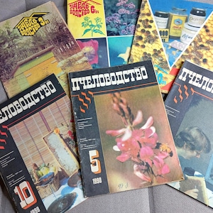 Op de afbeelding: Een verzameling van zes vintage tijdschriften getiteld Pchelovodstvo, met diverse omslagontwerpen waaronder foto's van bijenkorven, honingproducten, bloemenafbeeldingen en imkerapparatuur, met cyrillische tekst en nummers op elke omslag.