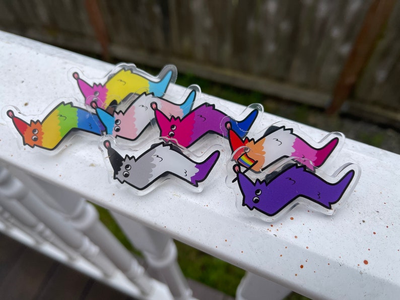 May include: A set of seven colorful worm-shaped pins with different expressions on their faces. The pins are made of clear acrylic and have a glossy finish.