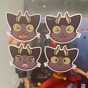 May include: Four stickers featuring a cartoon cat with horns and different facial expressions. The cat is purple with yellow horns and eyes. The stickers are on a white background.