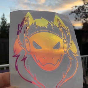 Könnte beinhalten: Ein holografischer Aufkleber mit einem Cartoon-Wolfskopf in einem gelben und rosa Farbverlauf. Der Wolf trägt Kopfhörer und hat einen wütenden Ausdruck.