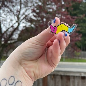 May include: A clear plastic sticker with a cartoon worm design. The worm is pink, yellow, and blue. The worm is smiling and has eyes.