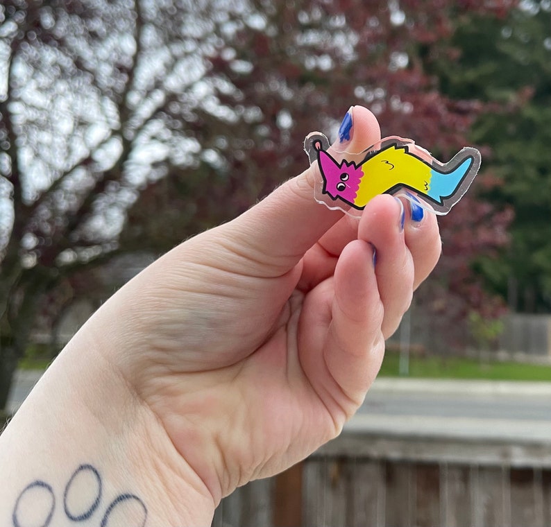 May include: A clear plastic sticker with a cartoon worm design. The worm is pink, yellow, and blue. The worm is smiling and has eyes.