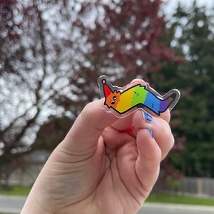 May include: A rainbow-colored worm sticker with a happy face and a party hat. The sticker is made of clear vinyl and has a glossy finish.