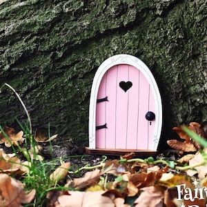 a small pink fairy door sitting under a tree