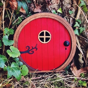 a red fairy door in the middle of the forest in front of a tree