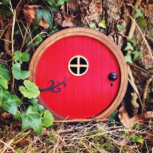 a red fairy door in the middle of the forest in front of a tree