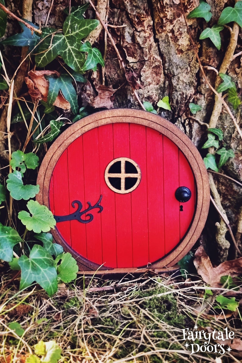 a red fairy door in the middle of the forest in front of a tree