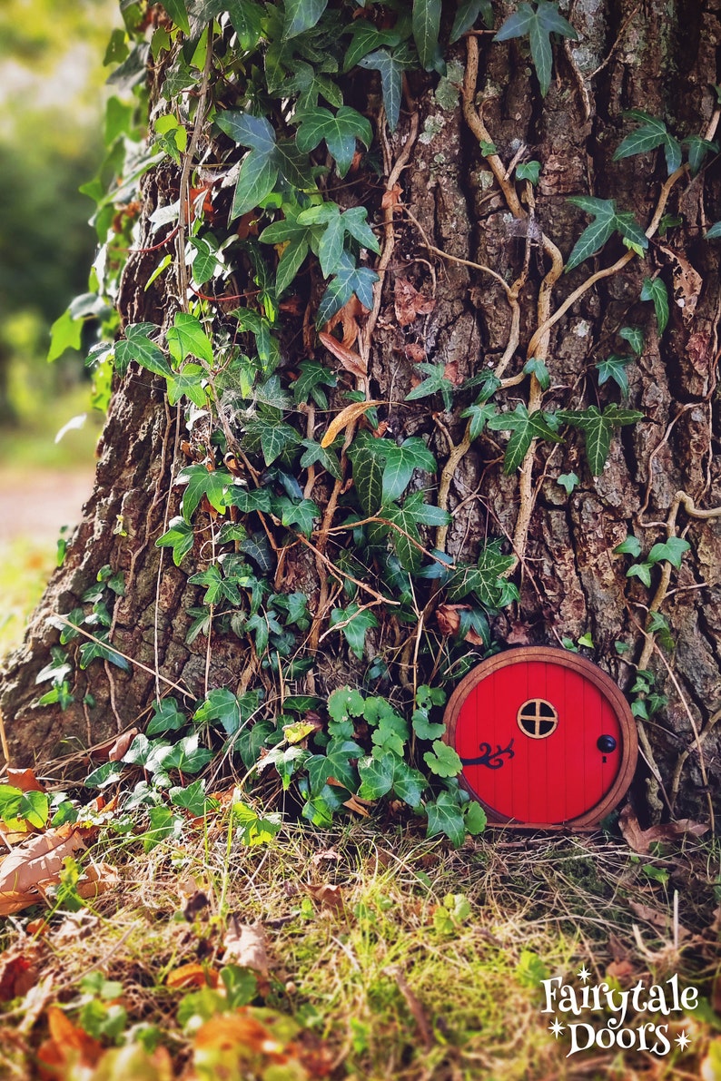 a red fairy door in the middle of the forest in front of a tree