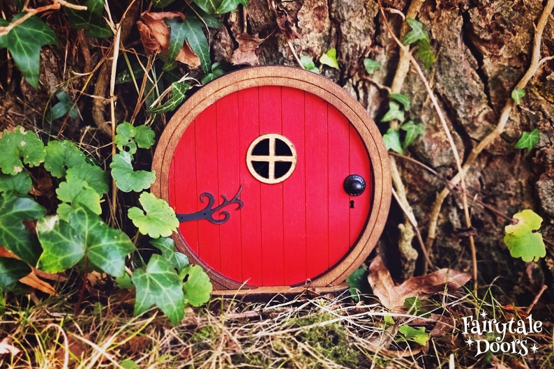 a red fairy door in the middle of the forest in front of a tree