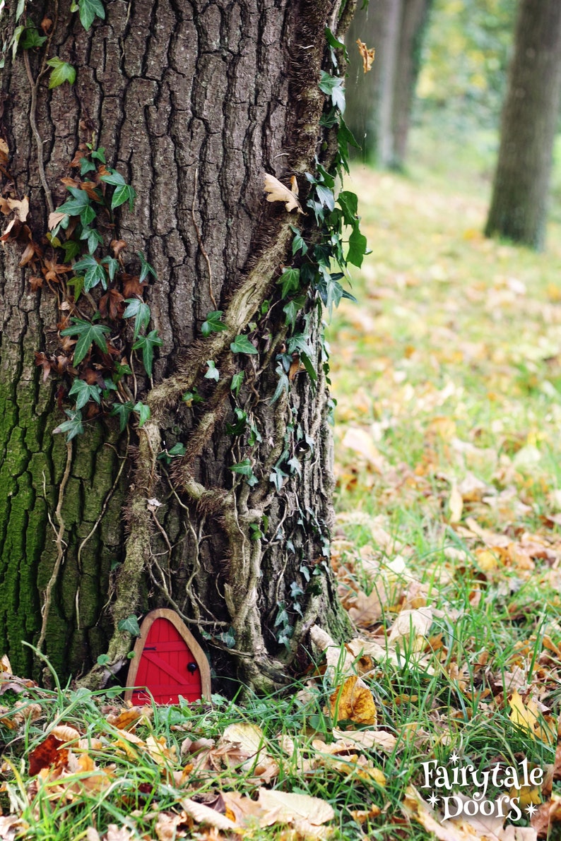 a red little fairy door sitting in front of a tree