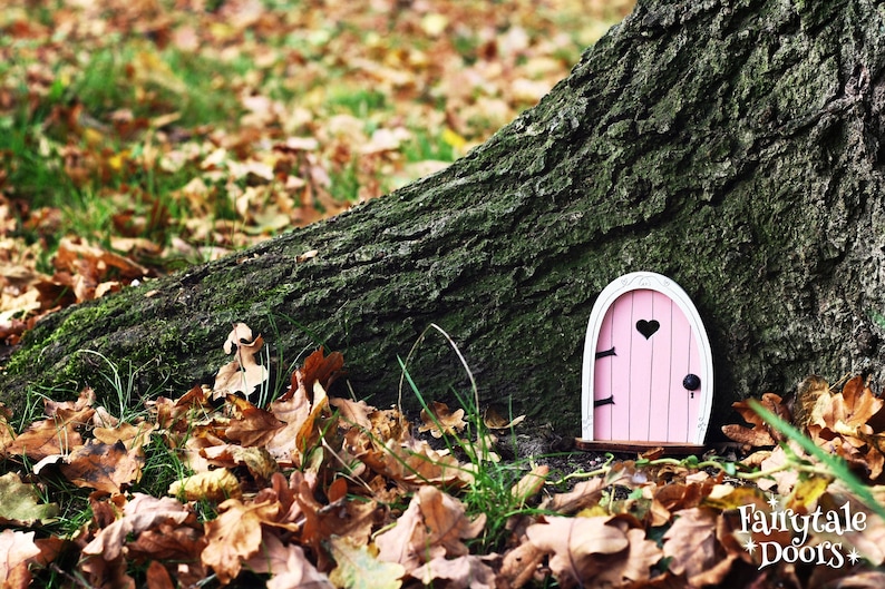 a small pink fairy door sitting under a tree