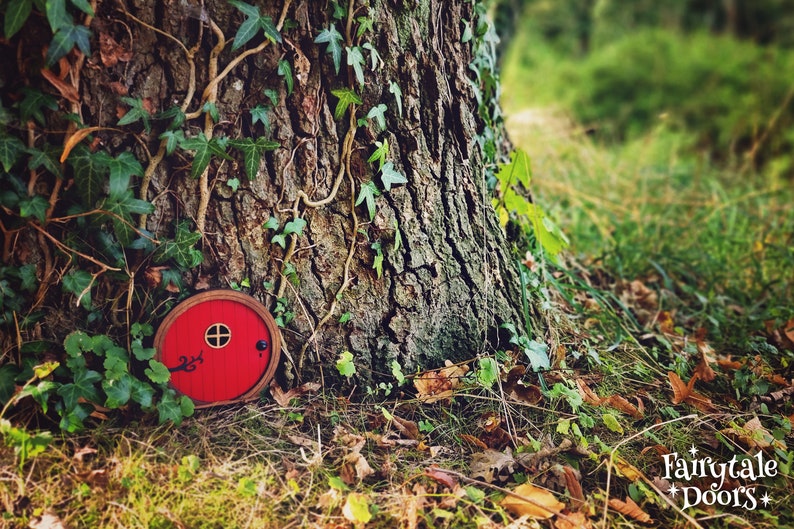 a red fairy door in the middle of the forest in front of a tree