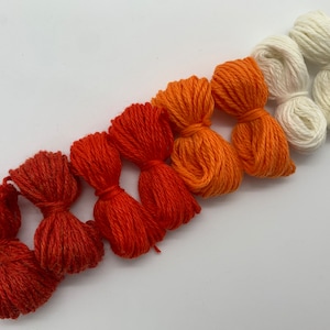Peut inclure: Un ensemble de huit écheveaux de fil dans des tons d'orange, de rouge et de blanc. Le fil est disposé en dégradé du blanc au rouge.
