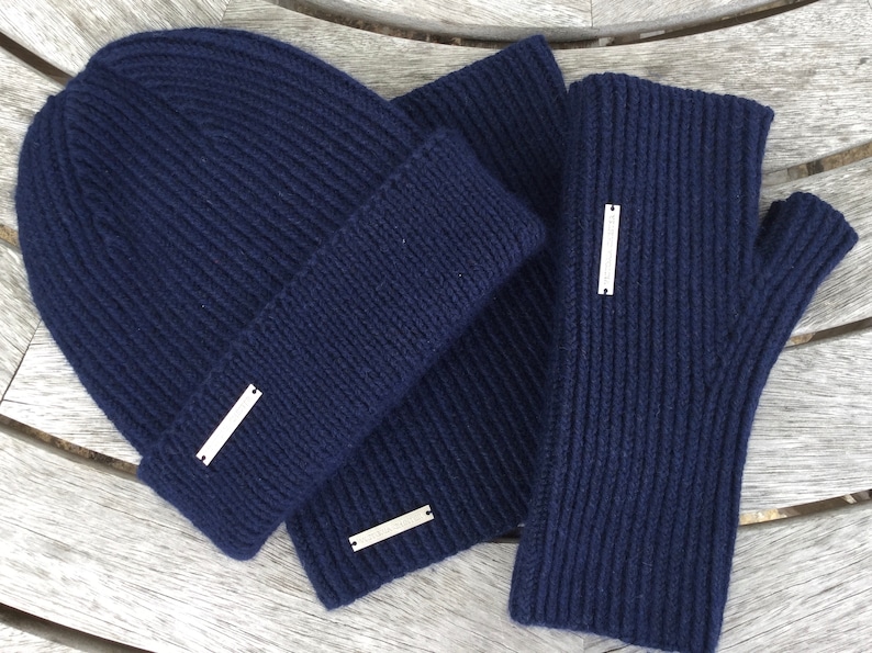 May include: A navy blue knit beanie, scarf, and fingerless gloves set. The set features a silver metal tag on each piece.