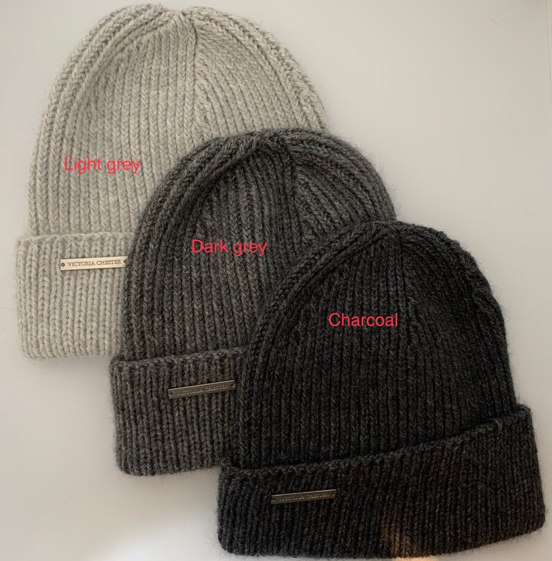 May include: Three knitted beanies in different shades of gray: light gray, dark gray, and charcoal. Each beanie has a small label with the text "Victoria Chester" on it.