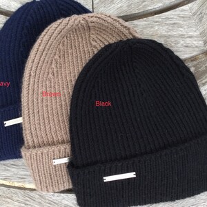 May include: Three knitted beanies in navy, brown, and black. Each beanie has a silver metal tag.