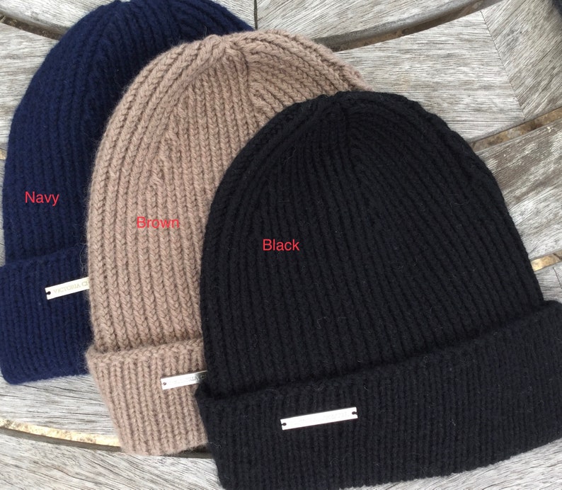 May include: Three knitted beanies in navy, brown, and black. Each beanie has a silver metal tag.