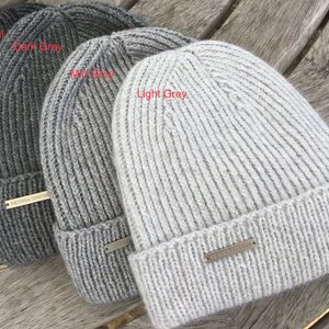 May include: Four knitted beanies in different shades of gray, from charcoal to light gray. Each beanie has a ribbed texture and a small metal tag with the text "VICTORIA SECRET" on it.