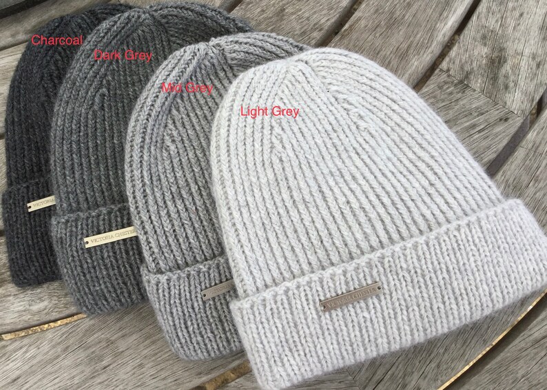 May include: Four knitted beanies in different shades of gray, from charcoal to light gray. Each beanie has a ribbed texture and a small metal tag with the text "VICTORIA SECRET" on it.