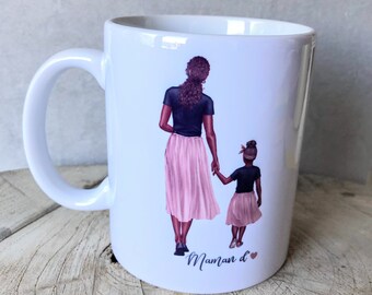 May include: White ceramic mug with a design of two women walking hand-in-hand. The woman in the front is wearing a pink skirt and a blue shirt. The woman in the back is wearing a pink skirt and a blue shirt. The text "Maman d" is printed on the mug.