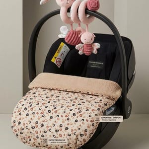 Könnte beinhalten: Ein schwarzer Babysitz mit einem beigen Fußsack mit Leopardenmuster und beigem Fleecefutter. Ein Spiral-Plüschspielzeug mit einem rosa Hasenkopf und einem rosa Schmetterling hängt am Griff. Textetiketten: CHALEUR ET CONFORT und ENTRETIEN FACILE.