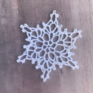 May include: A white crocheted snowflake ornament with a delicate, intricate design.