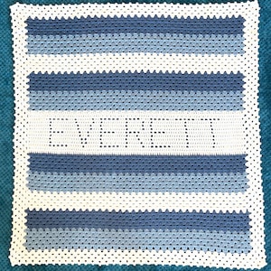 May include: A white crocheted baby blanket with blue stripes and the word "EVERGREEN" in the center.