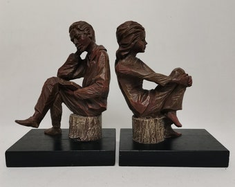 Puede incluir: Un par de sujetalibros con un hombre y una mujer sentados en tocones de árboles. Los sujetalibros están hechos de un material marrón oscuro y tienen un aspecto rústico.