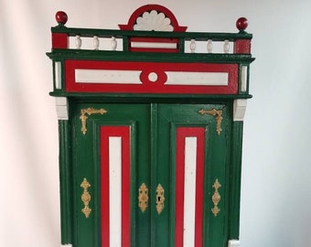 Small antique cabinet with two doors behind which shelves in green white and red gold ornaments 1940s Antique miniature cabinet folk art