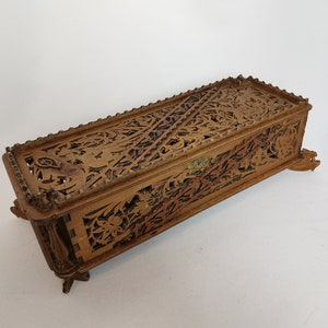 May include: A wooden box with intricate carvings of flowers and leaves. The box has a hinged lid and sits on four small feet.