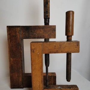 May include: Two wooden clamps with metal screws and handles. The clamps are made of dark brown wood and have a rustic appearance.