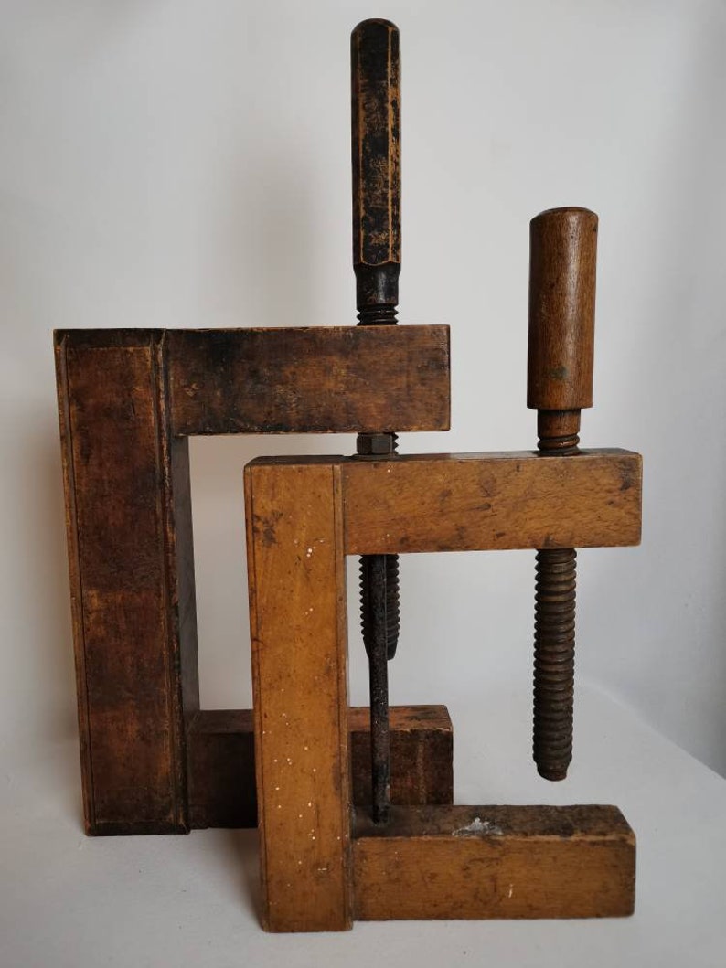May include: Two wooden clamps with metal screws and handles. The clamps are made of dark brown wood and have a rustic appearance.