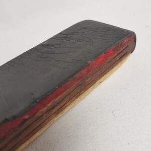 May include: A black rubber eraser with a red and wood layered base. The eraser is worn and has cracks in the surface.