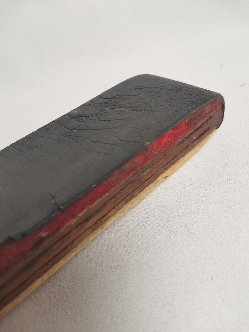 May include: A black rubber eraser with a red and wood layered base. The eraser is worn and has cracks in the surface.