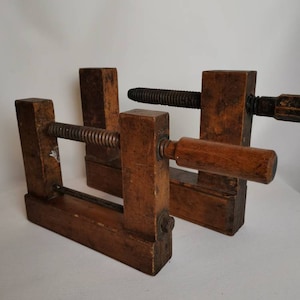 May include: Two vintage wooden clamps with a threaded metal screw and a wooden handle. The clamps are made of dark brown wood and have a rustic appearance.