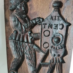May include: A wooden cookie mould with a carved design of a person holding a sign that says "One Cent".