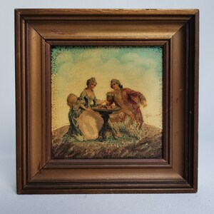 May include: A framed print depicting a scene with two figures in period clothing seated at a table. The artwork features a light blue sky background and is encased in a brown wooden frame, showcasing a vintage aesthetic.