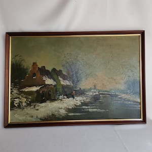Puede incluir: Una pintura al óleo enmarcada que representa una escena de invierno con un pequeño pueblo en primer plano. La pintura presenta un paisaje cubierto de nieve con un río helado y algunos árboles. El cielo es de un azul pálido con toques de rosa y naranja.