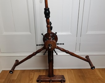 May include: Antique wooden yarn winder with a black and brown finish. The winder has a central wheel with spokes and four arms extending out to hold yarn spools. The winder sits on a wooden base with four legs.