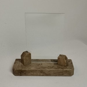 Può includere: Una cornice per foto in marmo marrone con un inserto in vetro trasparente. La cornice ha due pezzi decorativi in marmo scolpito sulla base.