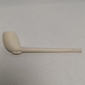 May include: A white ceramic pipe with a curved bowl and a long, straight stem.