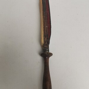 May include: A wooden knife sharpener with a brown wooden handle and a red, brown, and cream colored sharpening surface.