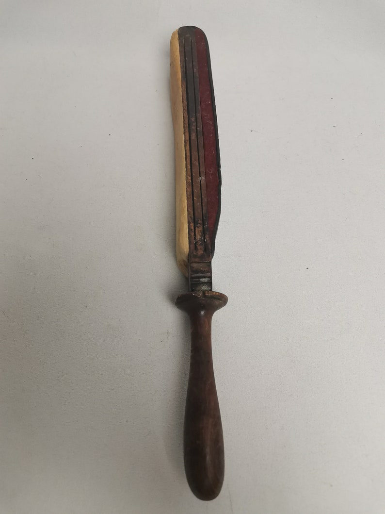 May include: A wooden knife sharpener with a brown wooden handle and a red, brown, and cream colored sharpening surface.