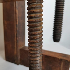May include: Close-up of a wooden clamp with a threaded screw. The screw is made of wood and has a dark brown finish. The clamp is made of two pieces of wood that are joined together by the screw.