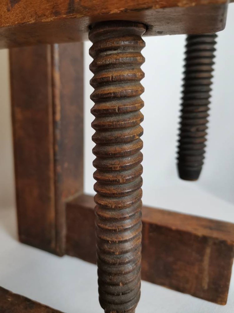 May include: Close-up of a wooden clamp with a threaded screw. The screw is made of wood and has a dark brown finish. The clamp is made of two pieces of wood that are joined together by the screw.