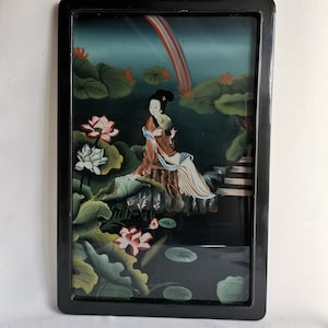 Può includere: Un dipinto incorniciato che raffigura una donna in abito tradizionale cinese seduta su uno scoglio circondata da fiori di loto e foglie. Lo sfondo è un cielo blu con un arcobaleno.