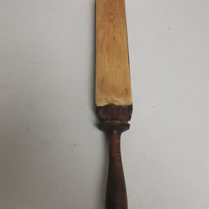 May include: A wooden strop with a light brown leather surface and a dark brown wooden handle.
